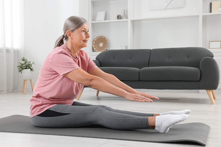 Senior woman in sportswear stretching on fitness mat